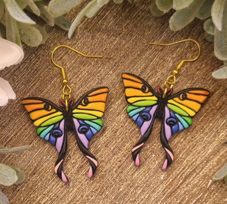 Vibrant butterfly-shaped earrings in rainbow colors, featuring intricate details and a glossy finish, hanging from gold hooks.