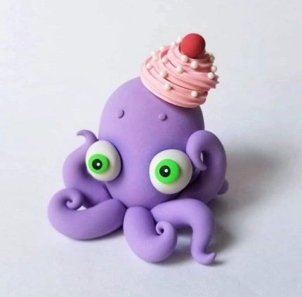 A cute purple octopus figurine with big green eyes, topped with a pink frosting cupcake and cherry, showcasing playful design and vibrant colors.
