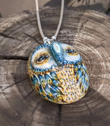 A detailed clay owl pendant featuring intricate patterns and vibrant colors, hanging from a light cord on a wooden surface.