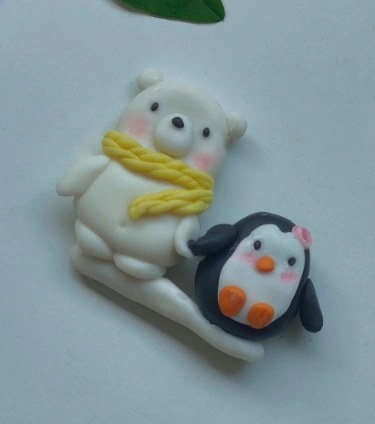 A cute clay sculpture featuring a white polar bear with a yellow scarf holding a black penguin with a flower.