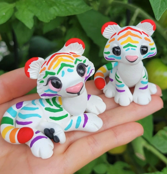 Two adorable clay tiger figurines with vibrant stripes; one is lying down, the other is sitting, both featuring large eyes and playful expressions.
